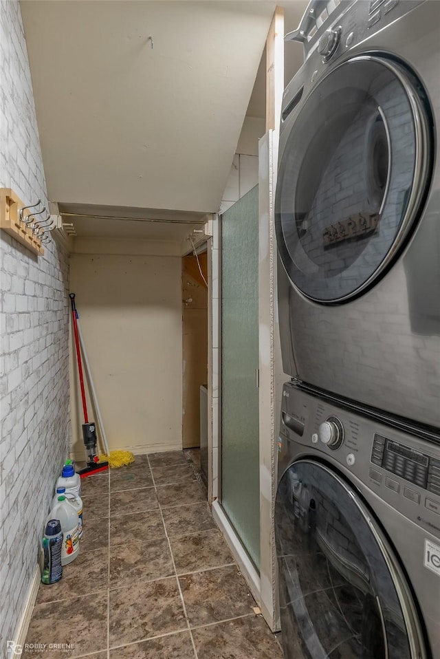 clothes washing area with brick wall and stacked washer / dryer