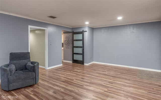 living area with a barn door, crown molding, and light hardwood / wood-style flooring