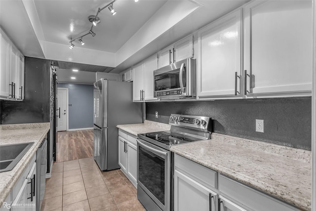 kitchen featuring light tile patterned flooring, tasteful backsplash, white cabinets, stainless steel appliances, and light stone countertops