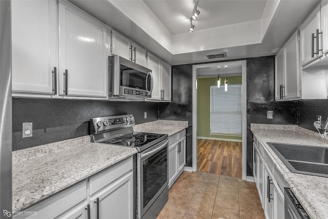 kitchen with appliances with stainless steel finishes, a tray ceiling, white cabinets, light tile patterned flooring, and decorative backsplash