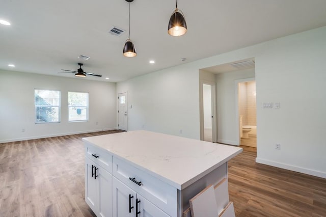 kitchen with pendant lighting, white cabinets, hardwood / wood-style flooring, a center island, and light stone counters