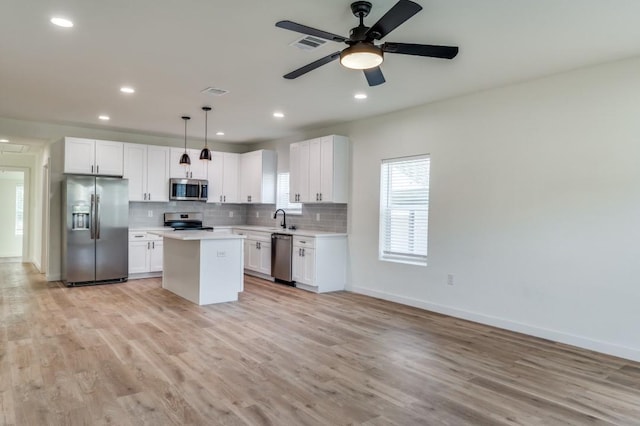 kitchen featuring sink, appliances with stainless steel finishes, white cabinetry, a center island, and decorative light fixtures