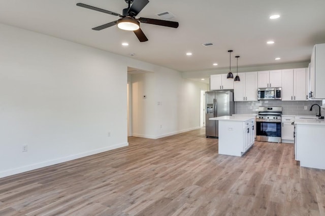 kitchen with sink, appliances with stainless steel finishes, a center island, white cabinets, and decorative light fixtures