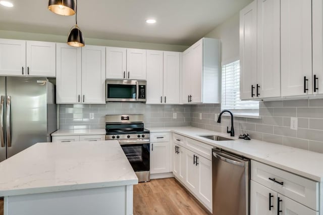 kitchen with stainless steel appliances, a center island, light stone counters, white cabinets, and decorative light fixtures