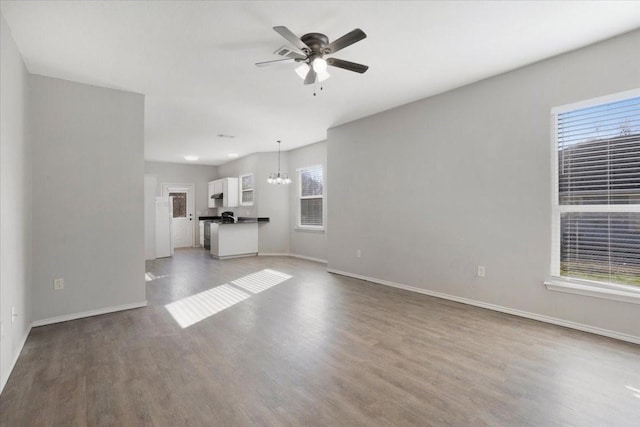 unfurnished living room featuring ceiling fan with notable chandelier, light wood-type flooring, and plenty of natural light