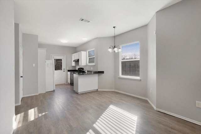 kitchen featuring pendant lighting, an inviting chandelier, black gas range, white fridge, and white cabinetry