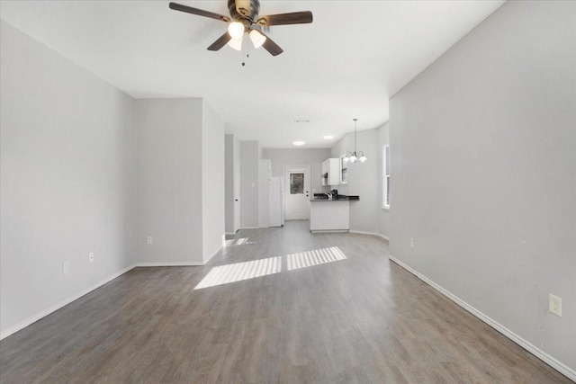 unfurnished living room featuring ceiling fan with notable chandelier and hardwood / wood-style flooring