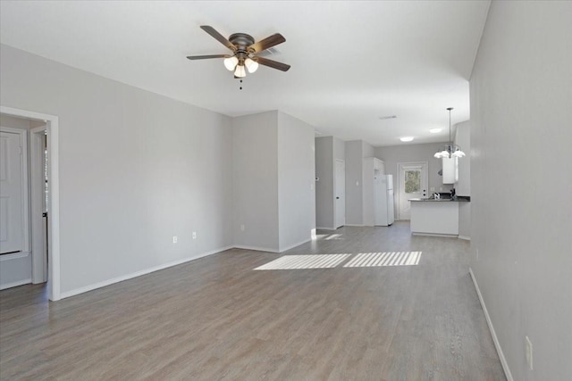 unfurnished living room with ceiling fan with notable chandelier and light hardwood / wood-style flooring