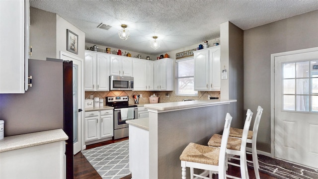 kitchen with a kitchen bar, kitchen peninsula, appliances with stainless steel finishes, dark hardwood / wood-style floors, and white cabinets