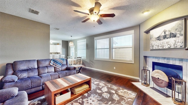 living room with ceiling fan, a textured ceiling, hardwood / wood-style flooring, and a tiled fireplace