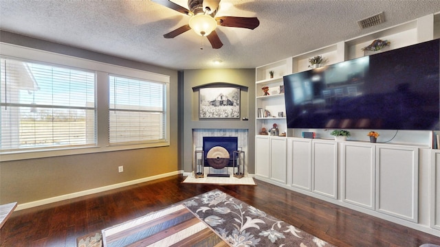 living room with a textured ceiling, dark hardwood / wood-style floors, a tiled fireplace, and built in shelves