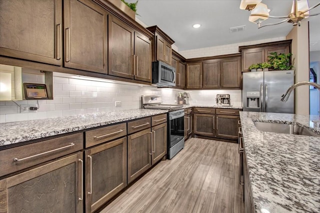 kitchen featuring light stone countertops, stainless steel appliances, sink, light hardwood / wood-style flooring, and an inviting chandelier