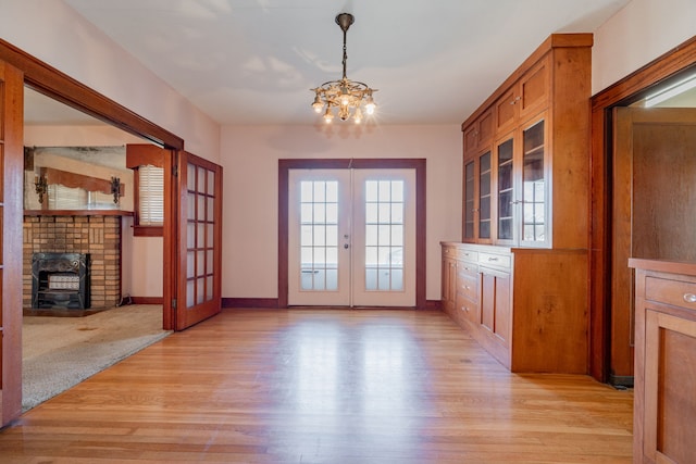 interior space with a wood stove, french doors, a chandelier, and light hardwood / wood-style floors