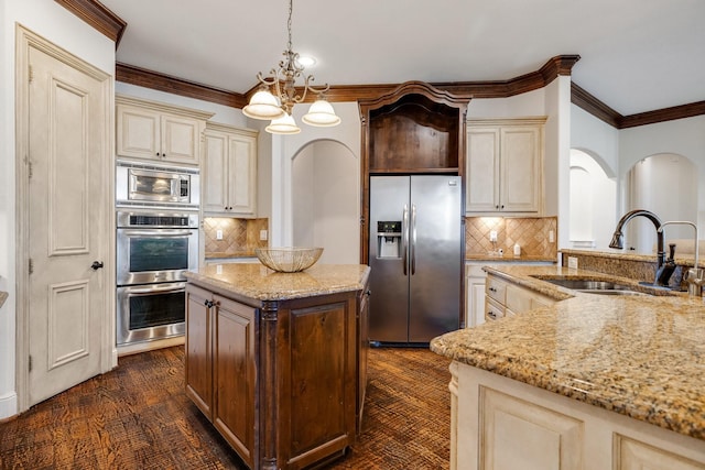 kitchen with backsplash, sink, hanging light fixtures, stainless steel appliances, and cream cabinetry