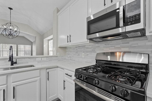 kitchen featuring appliances with stainless steel finishes, vaulted ceiling, sink, pendant lighting, and white cabinetry