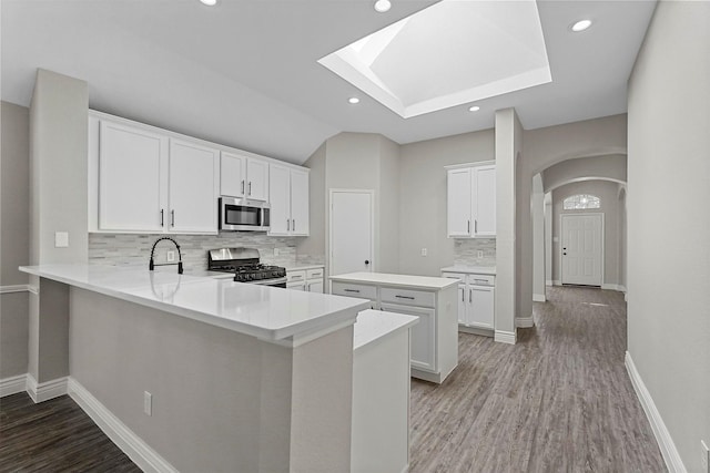 kitchen featuring white cabinets, kitchen peninsula, appliances with stainless steel finishes, and tasteful backsplash