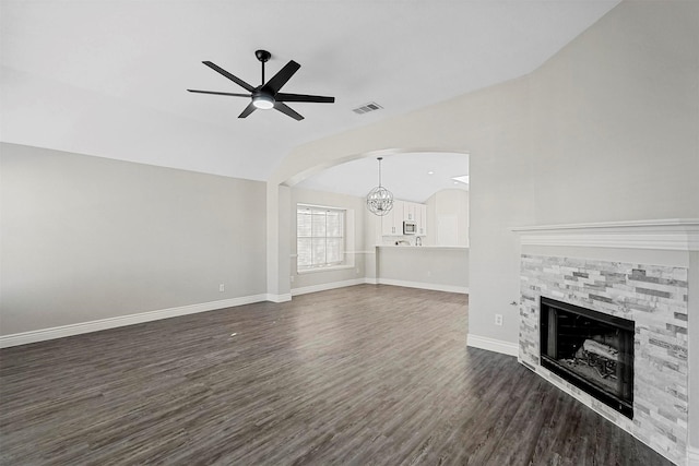 unfurnished living room featuring ceiling fan with notable chandelier, dark hardwood / wood-style flooring, vaulted ceiling, and a stone fireplace