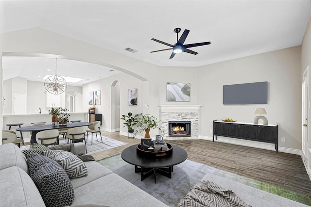 living room featuring ceiling fan with notable chandelier, wood-type flooring, and a tiled fireplace