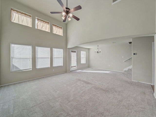 unfurnished living room with light colored carpet, a towering ceiling, and ceiling fan with notable chandelier