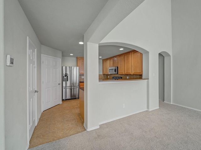 kitchen with tasteful backsplash, light colored carpet, kitchen peninsula, and stainless steel appliances