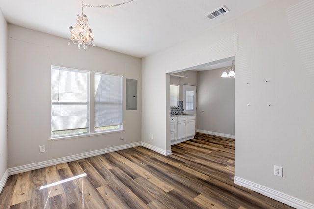 unfurnished dining area featuring electric panel, dark hardwood / wood-style floors, and an inviting chandelier