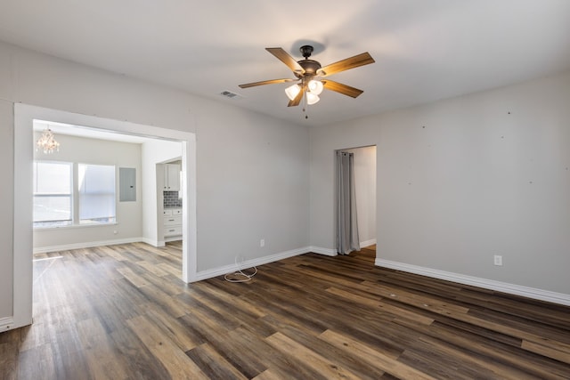 empty room featuring dark hardwood / wood-style floors, electric panel, and ceiling fan with notable chandelier