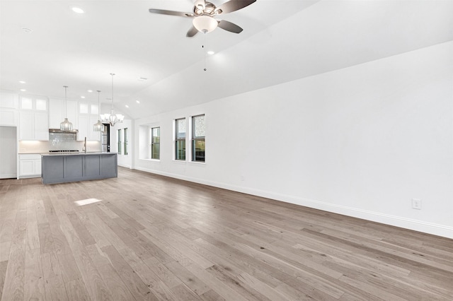 unfurnished living room with ceiling fan with notable chandelier, light hardwood / wood-style flooring, vaulted ceiling, and sink