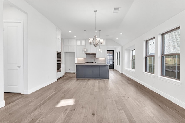 kitchen featuring stainless steel appliances, light hardwood / wood-style floors, white cabinetry, hanging light fixtures, and an island with sink