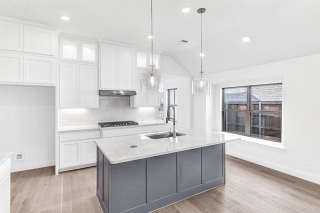 kitchen with sink, light stone counters, an island with sink, vaulted ceiling, and white cabinets