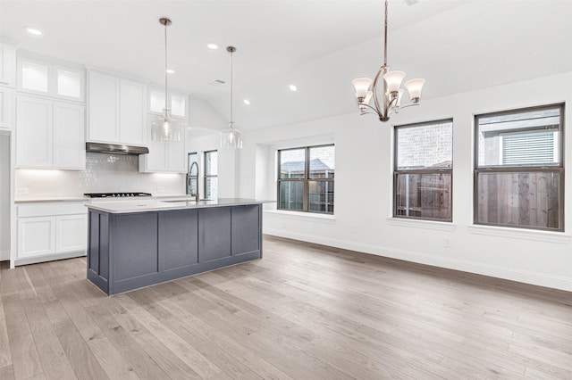 kitchen featuring pendant lighting, white cabinetry, an island with sink, and vaulted ceiling