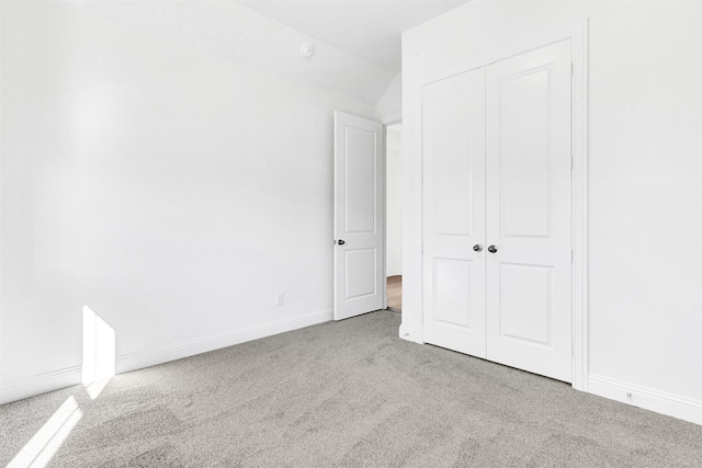 unfurnished bedroom with a closet, light colored carpet, and vaulted ceiling