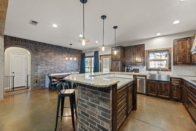 kitchen featuring pendant lighting, sink, a kitchen island, and brick wall