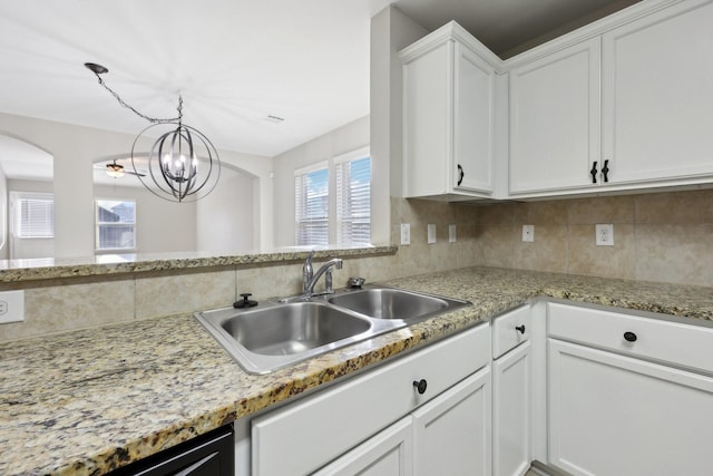 kitchen with tasteful backsplash, light stone counters, sink, pendant lighting, and white cabinetry