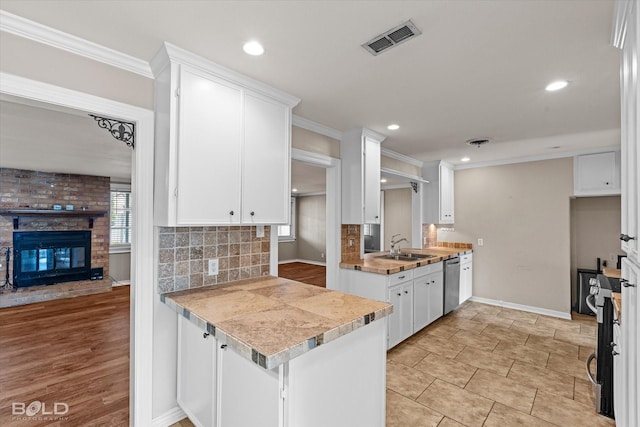 kitchen featuring white cabinetry, dishwasher, a healthy amount of sunlight, and a brick fireplace