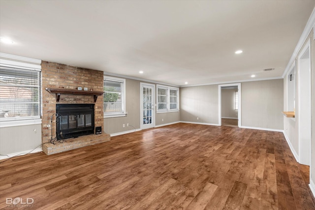 unfurnished living room featuring hardwood / wood-style floors, ornamental molding, and a brick fireplace