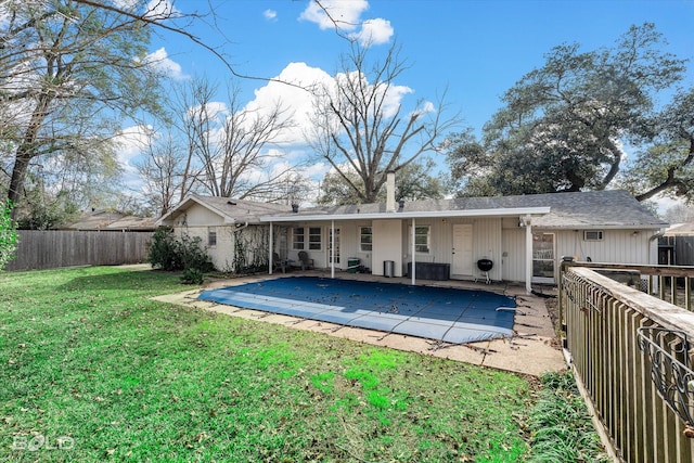 rear view of house featuring a lawn, a patio, and a covered pool