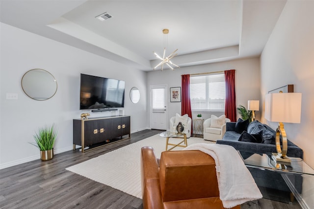 living room with a tray ceiling, dark wood-type flooring, and a notable chandelier