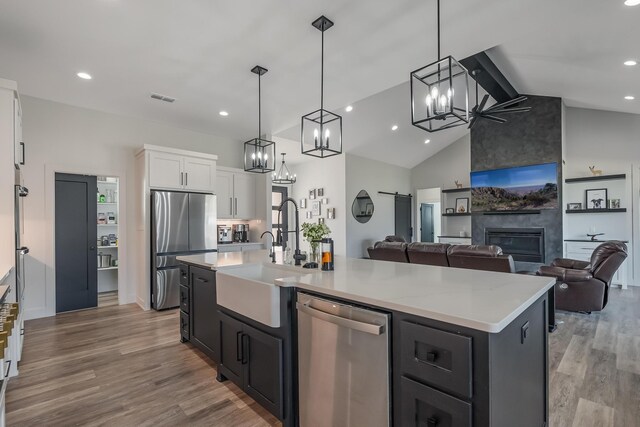 kitchen with white cabinetry, a large fireplace, decorative light fixtures, a kitchen island with sink, and appliances with stainless steel finishes