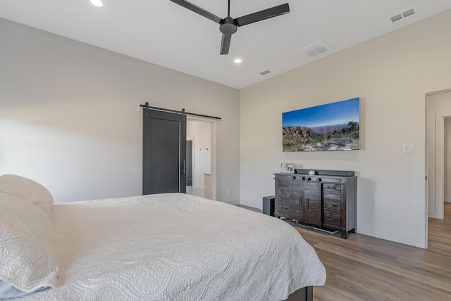 bedroom with a barn door, hardwood / wood-style flooring, and ceiling fan