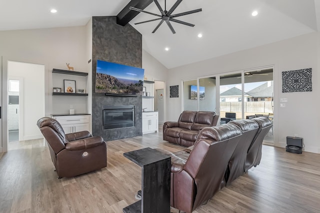 living room featuring ceiling fan, a large fireplace, light hardwood / wood-style flooring, beamed ceiling, and high vaulted ceiling