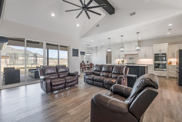 living room with ceiling fan, high vaulted ceiling, beam ceiling, and light hardwood / wood-style flooring