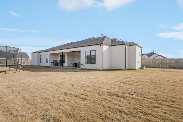 back of house featuring a trampoline, a lawn, and a patio