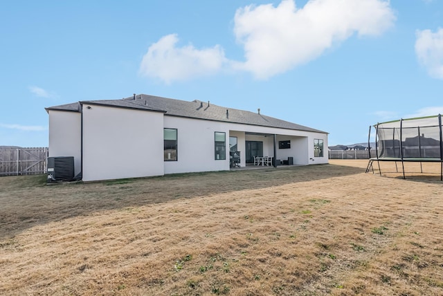 rear view of property with a patio, a trampoline, central air condition unit, and a lawn