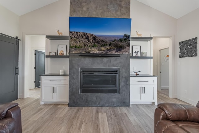 living room with lofted ceiling, a barn door, and light hardwood / wood-style flooring