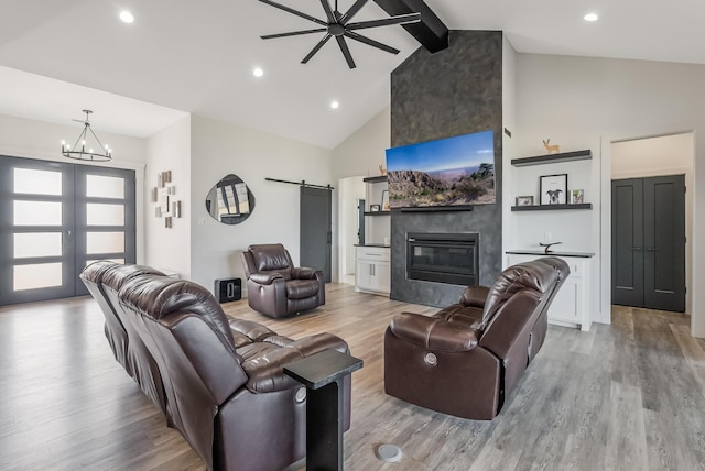 living room featuring ceiling fan with notable chandelier, a fireplace, beamed ceiling, a barn door, and light wood-type flooring