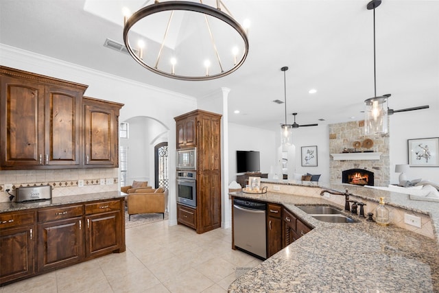 kitchen with sink, hanging light fixtures, a fireplace, appliances with stainless steel finishes, and ornamental molding