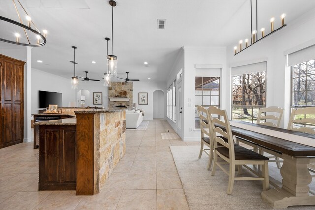 kitchen with a fireplace, stone countertops, pendant lighting, and ceiling fan with notable chandelier