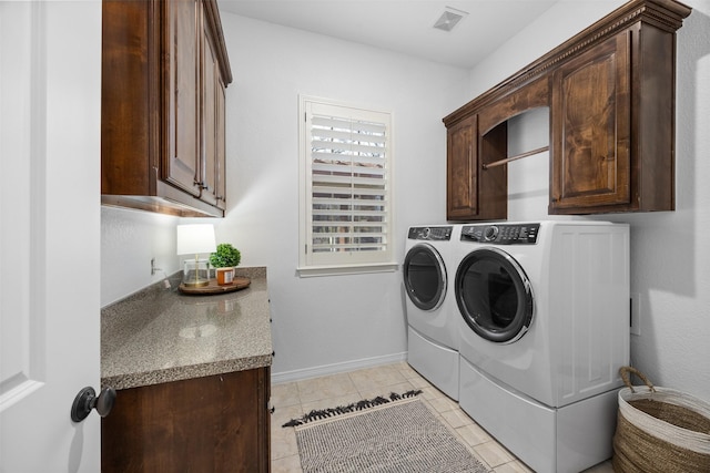 clothes washing area with cabinets, washing machine and dryer, and light tile patterned floors