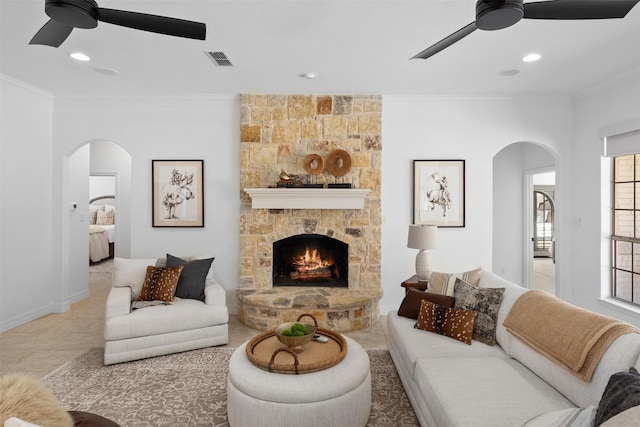 living room with crown molding, ceiling fan, and a stone fireplace