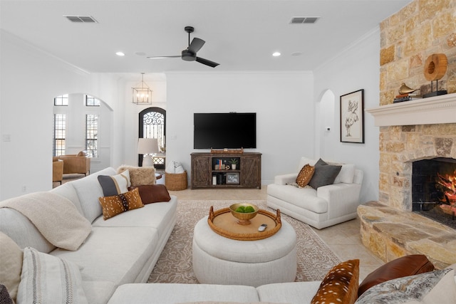 living room featuring light tile patterned floors, a stone fireplace, ceiling fan, and crown molding